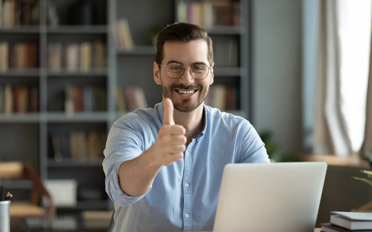 A man at his notebook laughs and gives a thumbs up