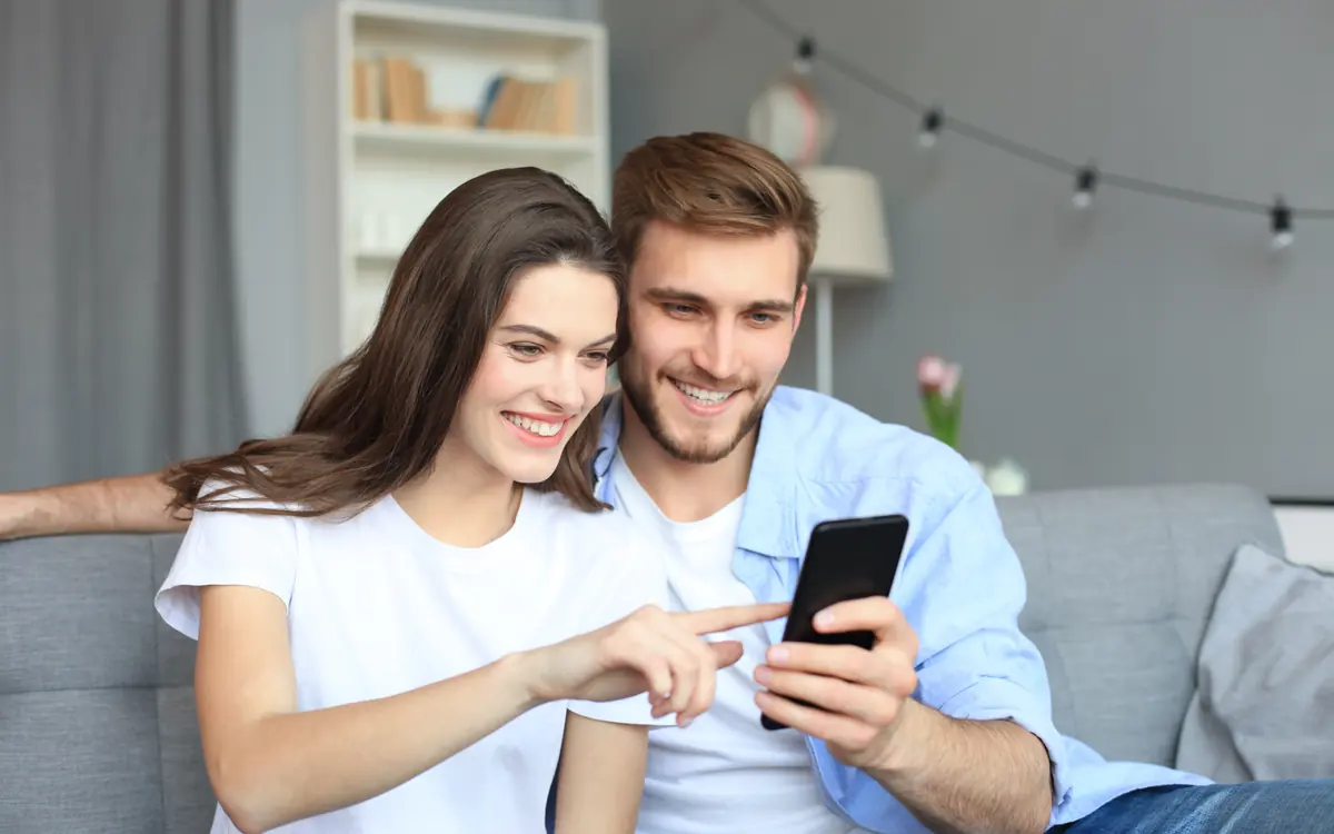A couple sits on the sofa looking at a phone together