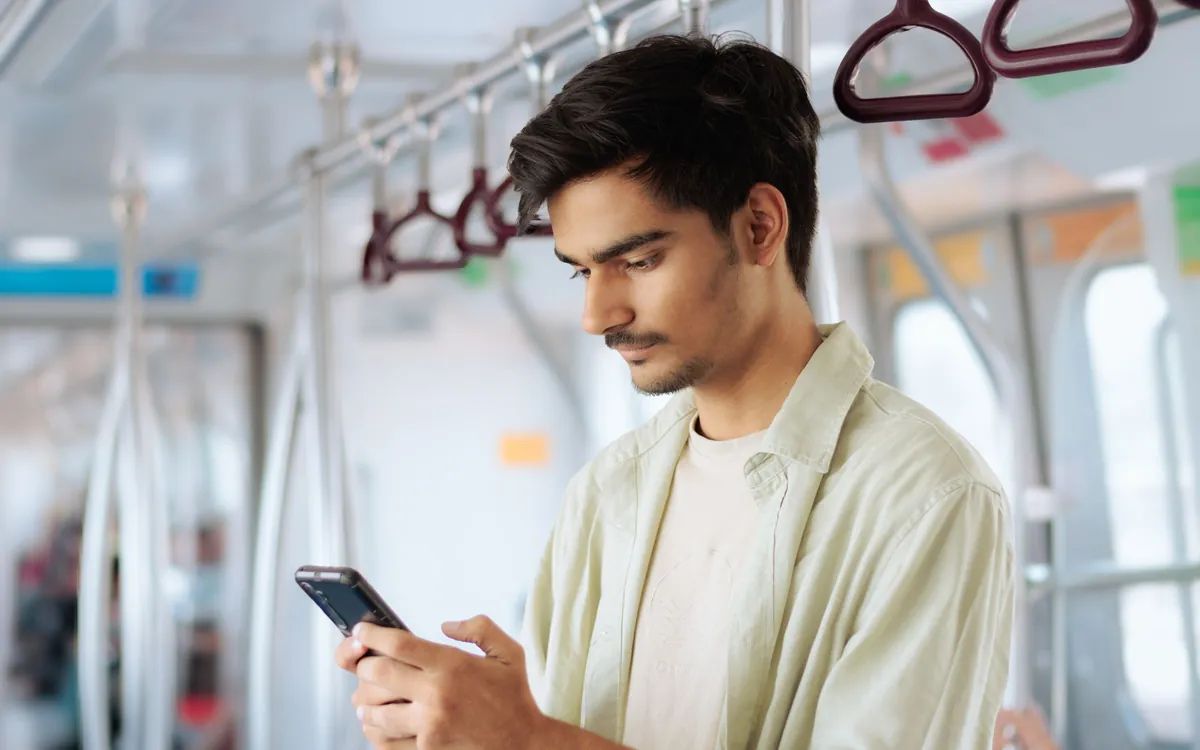 A young man stands on a train and looks at his phone