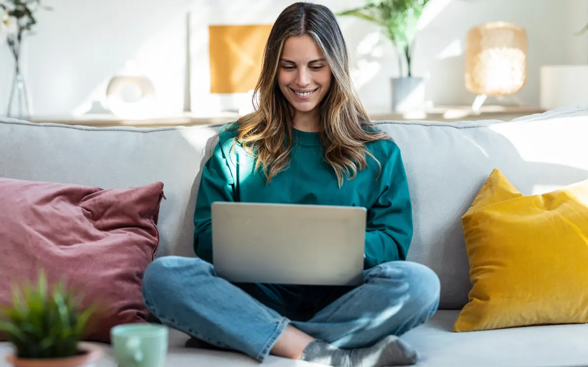 A woman in a green jumper sits on the sofa with her notebook